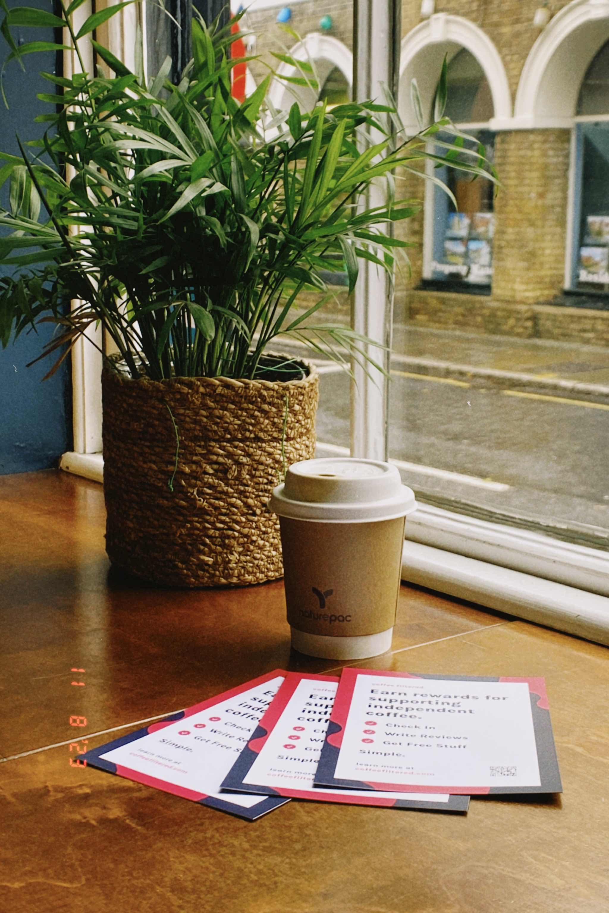 A picture of a takeaway coffee cup and with Coffee Filtered flyers sat alongside it.